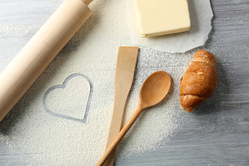 Fototapeta na wymiar Heart of flour, croissant and wooden kitchen utensils on gray background