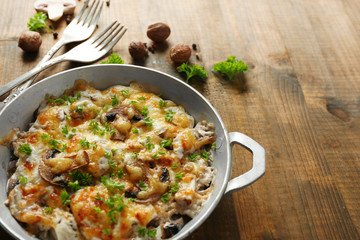 Roasted mushrooms, chicken and cheese gratin in pan, on wooden background