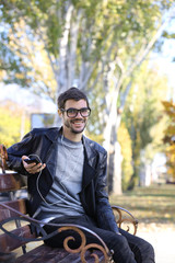 Young man sitting on a bench in park and listening to music