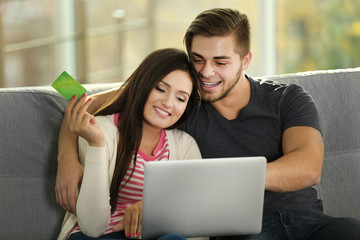 Young happy couple using credit card with laptop at home on light background