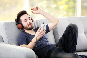 Fototapeta premium Handsome man emotionally listens music with headphones on grey sofa in the room