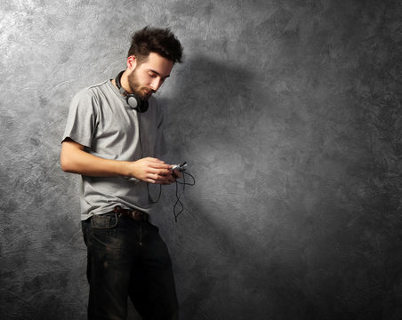 Young bearded man listening music with headphones on grey wall background