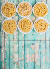 Various dried pasta variety and shapes in white bowl over wooden background