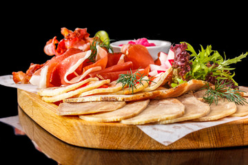 Sliced prosciutto, bacon and other deli meats lie on the board.
