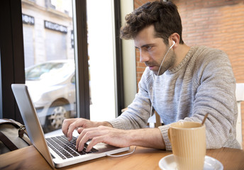 Young man listens to and write on computer with cup of coffee