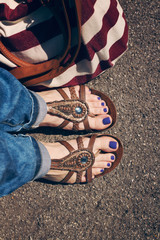 Women feet in summer flats with purple pedicure and with red and white stripped bag