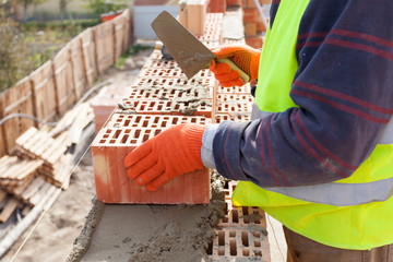 Construction mason worker bricklayer installing red brick with trowel putty knife outdoors