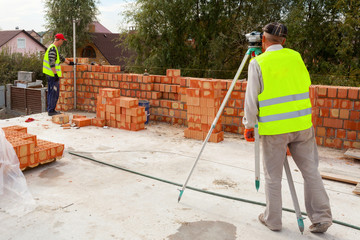 A worker with theodolite checks the validity of bricklaying