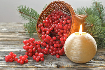Cornucopia with viburnum and candle on wooden background