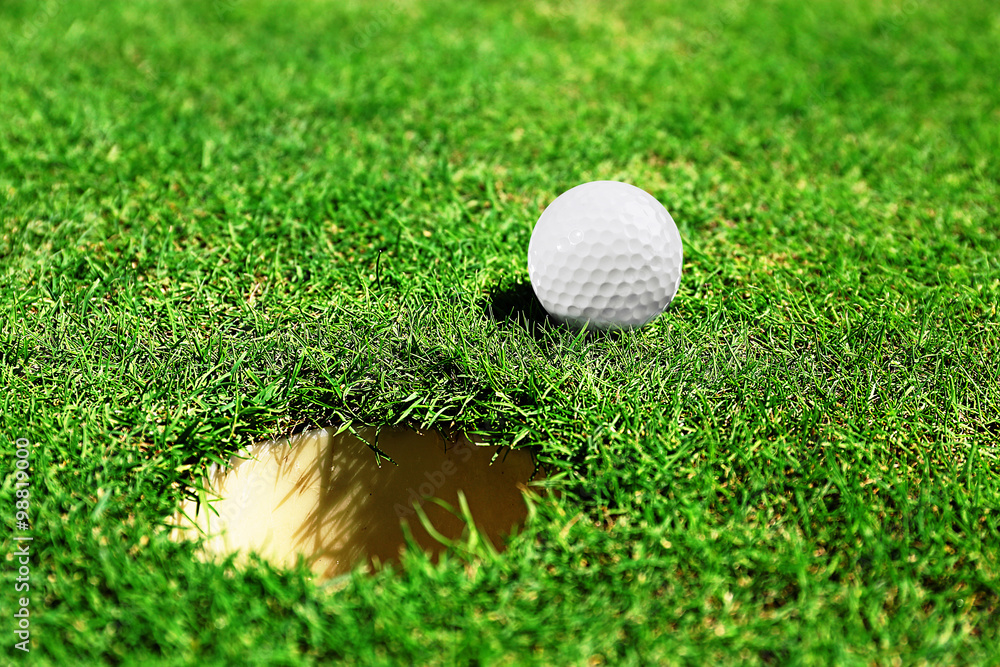 Wall mural Golf ball on lip of cup on the green golf course