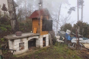 Homemade smokehouse in the morning mist. Domestic production of sausages. Smokehouse at the house in the woods. Traditional food
