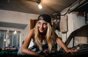 Fototapeta na wymiar young blonde girl with long hair is an auto mechanic in the garage with a lot of tools on the shelves holding wrenches