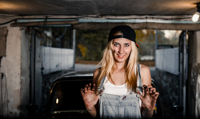 young blonde girl with long hair is an auto mechanic in the garage with a lot of tools on the shelves holding wrenches