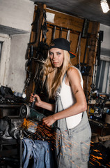 Obraz na płótnie Canvas young blonde girl with long hair is an auto mechanic in the garage with a lot of tools on the shelves holding wrenches