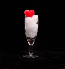 Transparent glass goblet with the red ice heart lying in snow. B