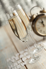 Glasses of champagne and alarm clock on wooden background