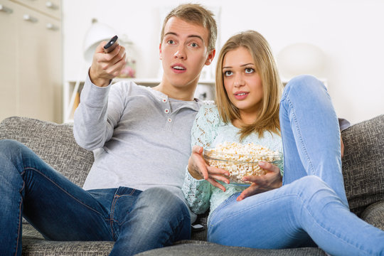 young couple watching tv and relaxing on sofa with pop corn
