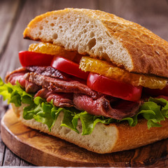 Juicy steak sandwich with vegetables and slices of orange.