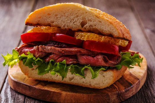 Juicy steak sandwich with vegetables and slices of orange.
