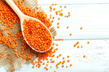 Red lentils in the wooden spoon on a blue wooden table