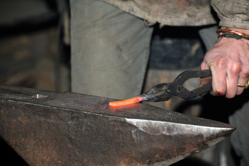 Detail shot of hammer forging hot iron at anvil