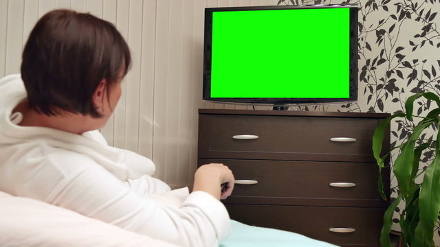 Woman watches green screened TV. Dolly shot.