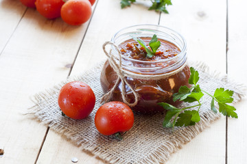 Tomato sauce (jam) in glass jar with parsley and fresh tomatos on dark wooden table, selective focus.