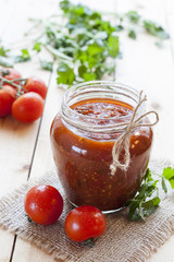Fototapeta na wymiar Tomato sauce (jam) in glass jar with parsley and fresh tomatos on dark wooden table, selective focus.