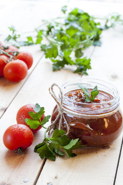Tomato sauce (jam) in glass jar with parsley and fresh tomatos on dark wooden table, selective focus.
