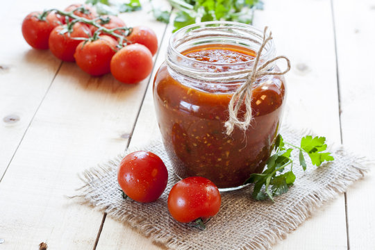 Tomato sauce (jam) in glass jar with parsley and fresh tomatos on dark wooden table, selective focus.