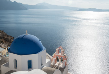Blue-domed Greek Orthodox church and pink bell tower overlooking the Aegean Sea in Oia town on the island of Santorini, Greece