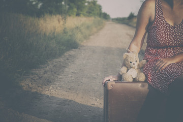 Traveler woman on the road with retro suitcase and teddy bear