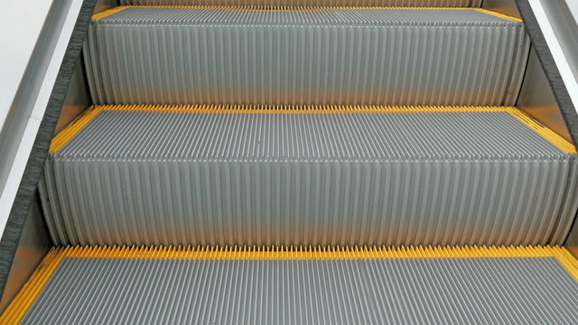 An escalator going up to a building. Closer look of the yellow lines and steps of the escalator