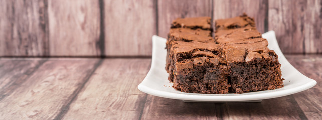 Homemade chocolate brownies in white plate over wooden background
