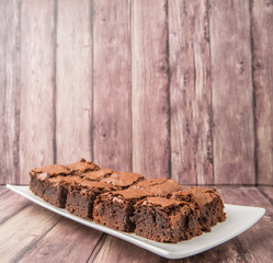 Homemade chocolate brownies in white plate over wooden background