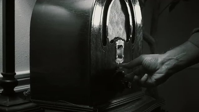 A man’s hand turns the dial on an old vintage 1940’s radio until he finds the music he is looking for, stops and starts tapping his finger. Film Noir