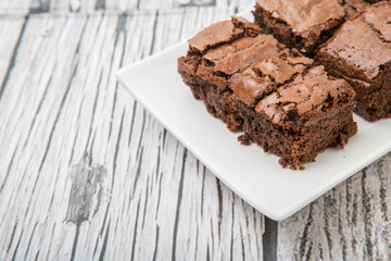 Homemade chocolate brownies in white plate over wooden background