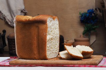 На столе свежеиспеченный хлеб. Огромная буханка белого хлеба, несколько отрезанных кусков хлеба. Хлеб крупным планом