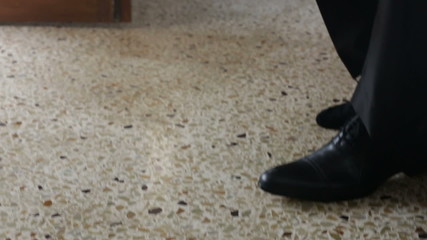 man in white wedding shirt puts on black shoes ties shoe-laces
