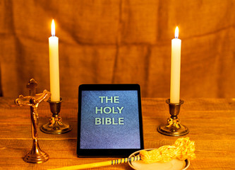 Digital holy bible as a symbol of a new era. Scene from the cross, candles and sprinkler.
