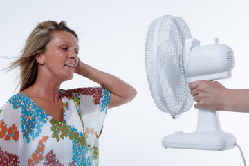 Woman is cooled down by a handheld fan (against white studio back ground)