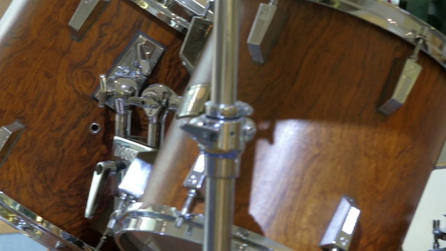 A bass drum with brown color inside a room. A bass drum is a large drum that produces a note of low definite or indefinite pitch.