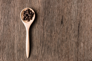 Coffee beans in wood spoon on wood table.