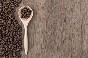 Coffee beans in wood spoon on wood table.