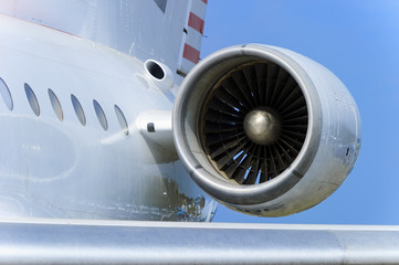 Engine on white fuselage with portholes of passenger plane, jet turbine, windows, hull and wing, aircraft detail, aviation and aerospace industry, blue sky on background 