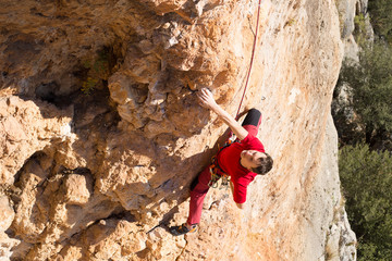 Young male climber hanging by a cliff.