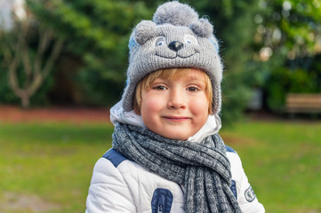 Outdoor close up portrait of a cute little boy wearing funny hat and scarf