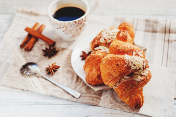 sweet breakfast or lunch, a cup of black coffee and croissants with almonds , nuts and cinnamon on a wooden background