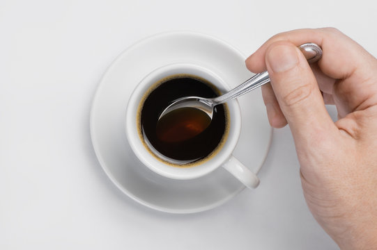 Male Hand Stir Slowly Black Coffee With Spoon In Coffee Cup Against White Background With Place For Text Top View