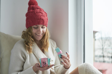 Young woman with red hat holding her present near window